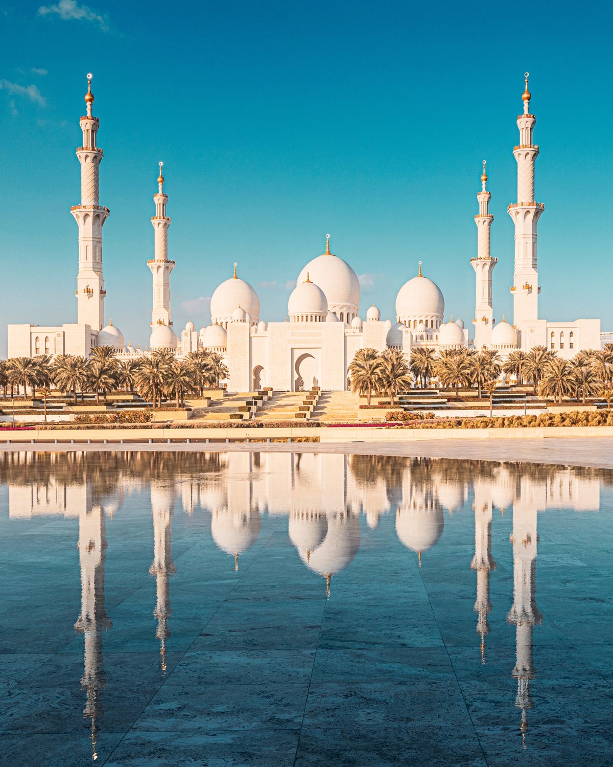 Sheikh Zayed Grand Mosque domes reflected in the courtyard pool, Abu Dhabi skyline in the distance